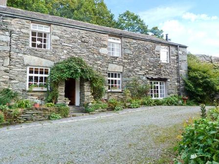 A stone cottage with plants around the entrance and windows surrounded by trees at High Kiln Bank Cottage Seathwaite Duddon Valley