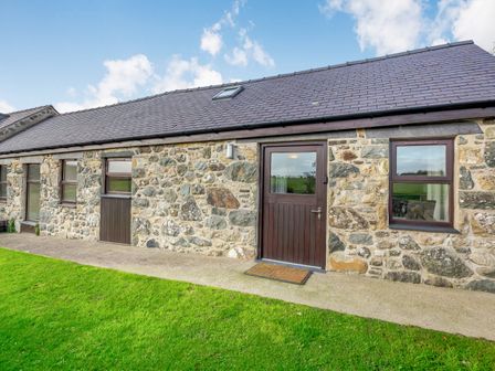 A stone building with multiple windows a door and a grassy lawn at Bwythyn-y-Saer in Abersoch