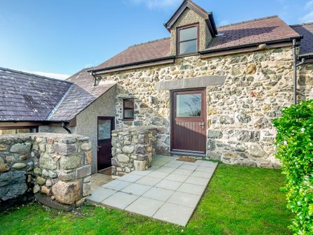 Stone exterior wall with two dark wooden doors and small patio area with tiled floor at Bwythyn-y-Wennol in Abersoch