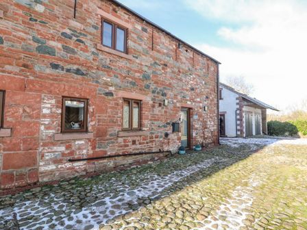 The exterior of a stone building with cobblestone ground and a smaller adjacent building at Blencathra Barn in Penrith