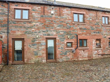 Stone exterior of a building with multiple brown framed windows and two glass doors at Saddleback Barn Newton Reigny near Penrith