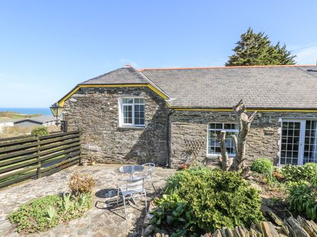 An outdoor stone patio with a metal table and chairs surrounded by plants next to a stone house at The Garden Apartment in Tintagel
