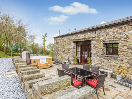 An outdoor patio with a dining table and chairs and a hot tub beside a stone building at Hill Side Barn Pennington near Ulverston