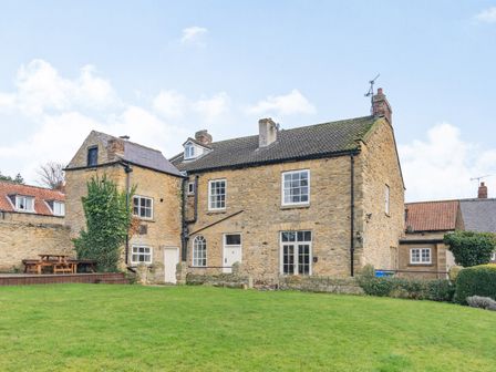 A stone house with multiple windows and a green lawn in front at The Lodge in Snainton near Scarborough