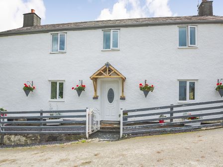 A white house with a wooden porch over the door and flower pots hanging on the wall at Ty Nant in Betws-y-Coed
