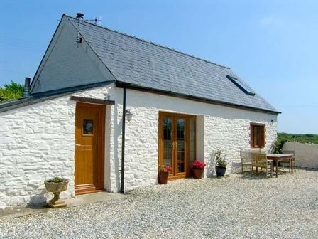 A white stone cottage with wooden door and windows and outdoor seating at Foxglove Cottage in Little Haven near Haverfordwest