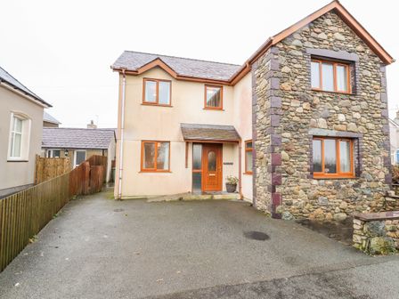 A stone and plaster house with wooden framed windows and a driveway at Bryn Seion in Y Felinheli