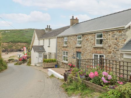 A stone cottage with flowers in raised beds beside a road near a beach at Hillbrook House in Nolton Haven