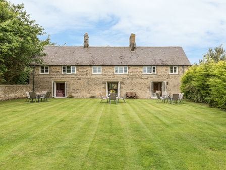 A stone cottage with three sets of open doors leading to a lawn with tables and chairs at Dorothy's Cottage in Alnmouth