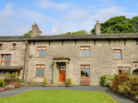 Stone house with wooden door and windows fronted by green lawn and gravel path at Longwell House in Selside near Kendal