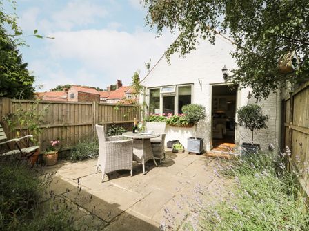 A small patio garden with a round table, two chairs, potted plants, and a wooden fence at The Old Forge in Stillington