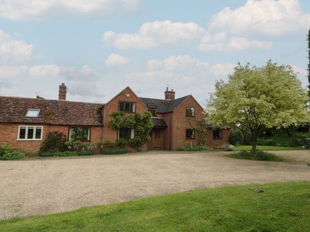 A brick house with a gravel driveway and a tree in front at Highcroft in Stratford-Upon-Avon