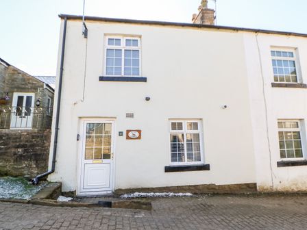 The front exterior of a white two-story cottage with three windows and a door at Kings Cottage in Alston