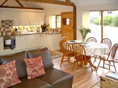 An open kitchen and dining area with wooden chairs around a table with a white cloth and a vase of flowers at Happy Union Stables in Abbeycwmhir near Rhayader