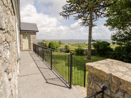 A stone house entrance with a metal railing next to a garden and a view of a body of water at Prague House in Lettermore County Galway