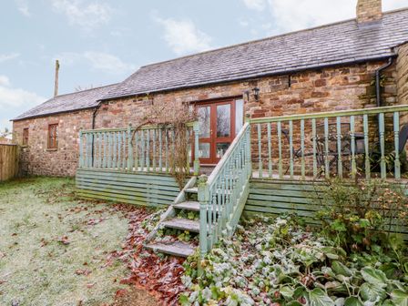 A stone house with a green wooden deck and stairs leading to glass doors at The Byre in Milton near Brampton