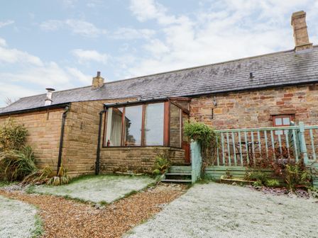 A stone cottage with a small porch and a garden with frosted grass and plants at The Stable in Milton near Brampton