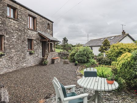 A stone house with gravel yard and outdoor table with chairs surrounded by bushes at Hollins Farm Barn New Hutton near Kendal