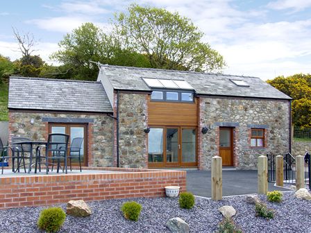 A stone house with a tiled roof and glass doors with outdoor seating on a raised patio at Ysgubor Penrallt in Y Felinheli near Caernarfon