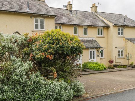 A row of beige townhouses with slate roofs and small bushes in front at Bramble Cottage in Sedbergh