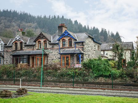 A row of stone cottages next to railway tracks with forested hills in the background at No 1 Railway Cottages in Betws-y-Coed