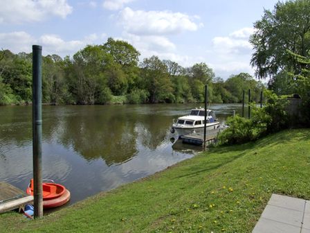 A river with a docked boat and an orange round boat on the shore at Rosewaters Cottage in Astley Burf near Stourport-on-Severn