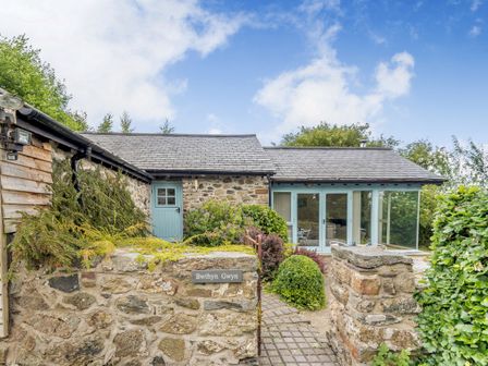 An exterior view of a stone cottage with blue wooden doors and a stone wall with a sign Bwthyn Gwyn in Penmynydd