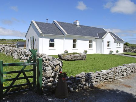 A white house with a slate roof surrounded by stone walls and a green gate at Dolmen Cottage in Carron near Kilfenora County Clare