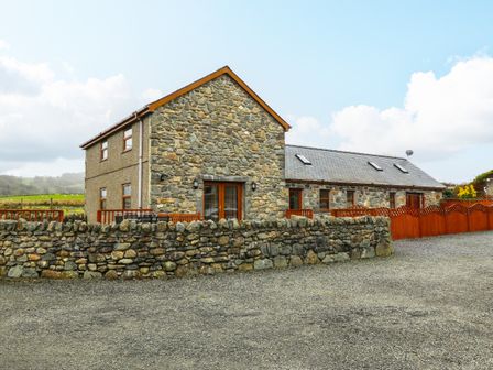 A stone house with wooden framed windows and a gravel driveway surrounded by a low stone wall at Cefn-Yr-Efail in Golan near Porthmadog