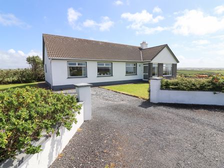 A white bungalow with a tiled roof and a driveway surrounded by low walls and bushes at Goodlands Cottage in Spanish Point County Clare