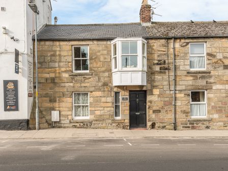 Stone facade house with black door and bay window above at Jackson Cottage in Alnmouth