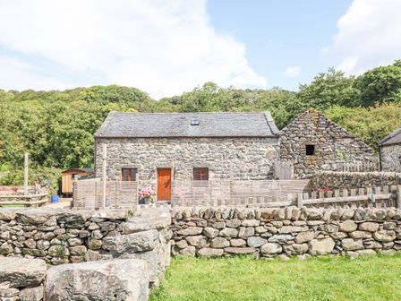 A stone house with wooden door and windows behind a stone wall with trees in the background at Isallt Llanfair near Harlech