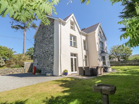 A stone and white exterior house with outdoor dining furniture on grass at Tyddyn Goronwy in Talybont