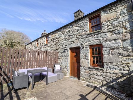 An outdoor patio area with a stone wall cottage wooden door wooden windows and outdoor seating at Cwm Yr Afon Cottage in Llanbedr near Harlech