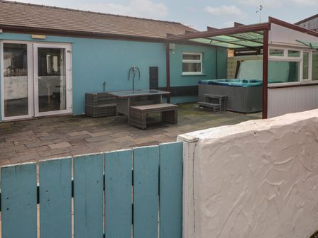 A patio with a hot tub table bench and blue wooden fence at Barn Cottage in Laugharne