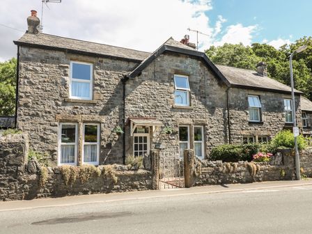 A stone house with white framed windows and a small metal gate in front at Riverside View in Cark in Cartmel