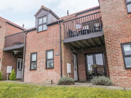 Exterior view of a brick townhouse with white doors balconies and a grass lawn at Cricket Cottage in Whitby