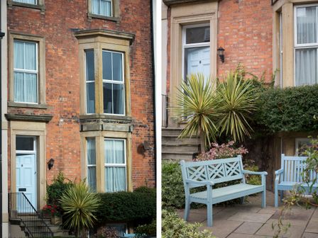 A brick house with a light blue door and windows with stone trim a paved front area with blue wooden benches and green plants at 6 Abbey Terrace Whitby