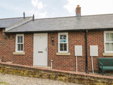 Front view of a brick cottage with a white door and two windows and a green bench outside at Clickety-Clack Cottage in Whitby