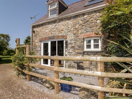 A stone cottage with a wooden fence and small outdoor seating area at The Coach House in Wolfscastle