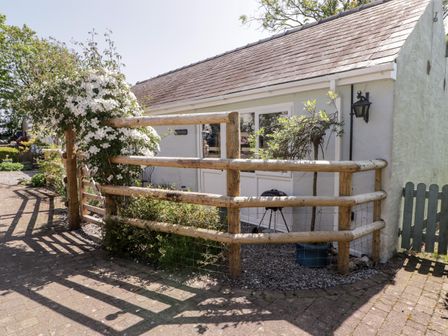 A small white building with wooden fencing and a flowering plant near the entrance at The Duck House in Wolfscastle