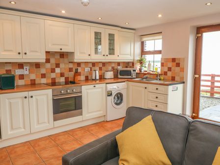 A kitchen with white cabinets washing machine oven microwave and a gray sofa with a yellow pillow at Cahirkeen Cottage Cahirkeen near Allihies County Cork