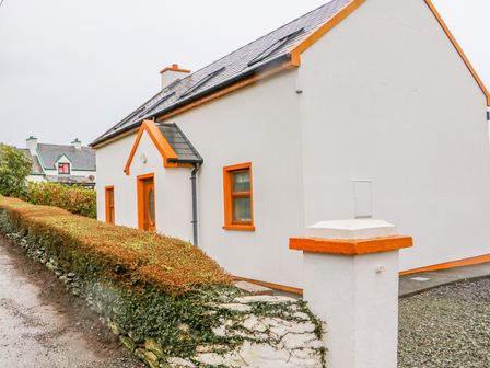 A white house with orange trim around windows and doors next to a hedge at Mary Agnes Cottage in Cahirkeen near Allihies County Cork