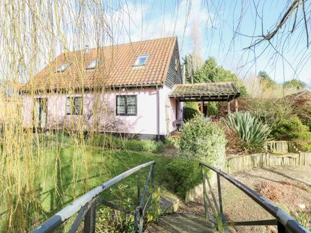 A house with a tiled roof and pink walls surrounded by a garden and a small bridge at The Haybarn in Necton near Swaffham