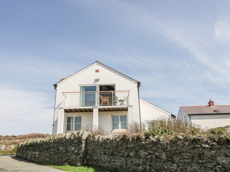 A white two-story house with a balcony and stone wall in front at Seascape in Trearddur Bay