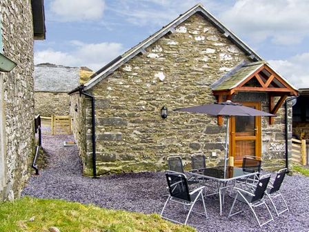 An outdoor patio area with a table umbrella and six chairs beside a stone building at Ty Isaf Penrhyddion Capel Garmon near Betws-y-Coed