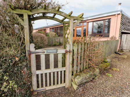 A wooden garden gate with a trellis and a sign reading Nuthatch leading to a path and a building with wooden windows at Nuthatch High Head Castle Farm Ive Valley near Penrith