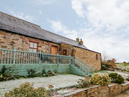 An exterior view of a stone house with a green wooden deck and stairs in a garden at The Dairy in Milton near Brampton