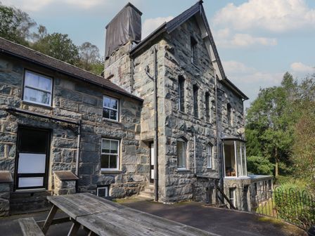 An exterior view of a stone building with multiple windows and a picnic table in the foreground at Bryn Cemlyn in Ganllwyd near Dolgellau