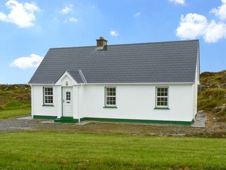 A white cottage with a gray roof and three windows on a grassy plot at Lully More Cottage in Cruit Island County Donegal